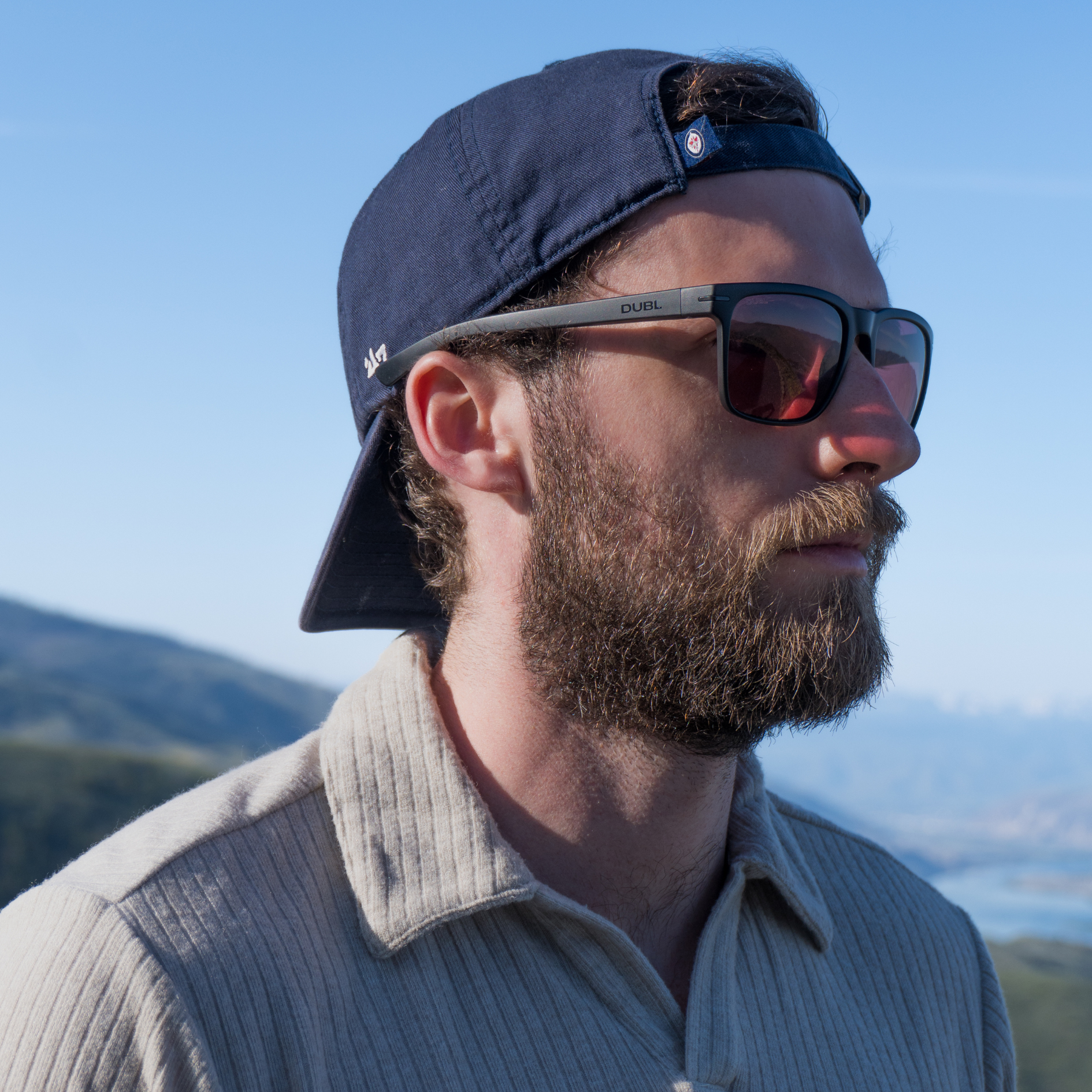 Man wearing sunglasses and a cap with mountains in the background