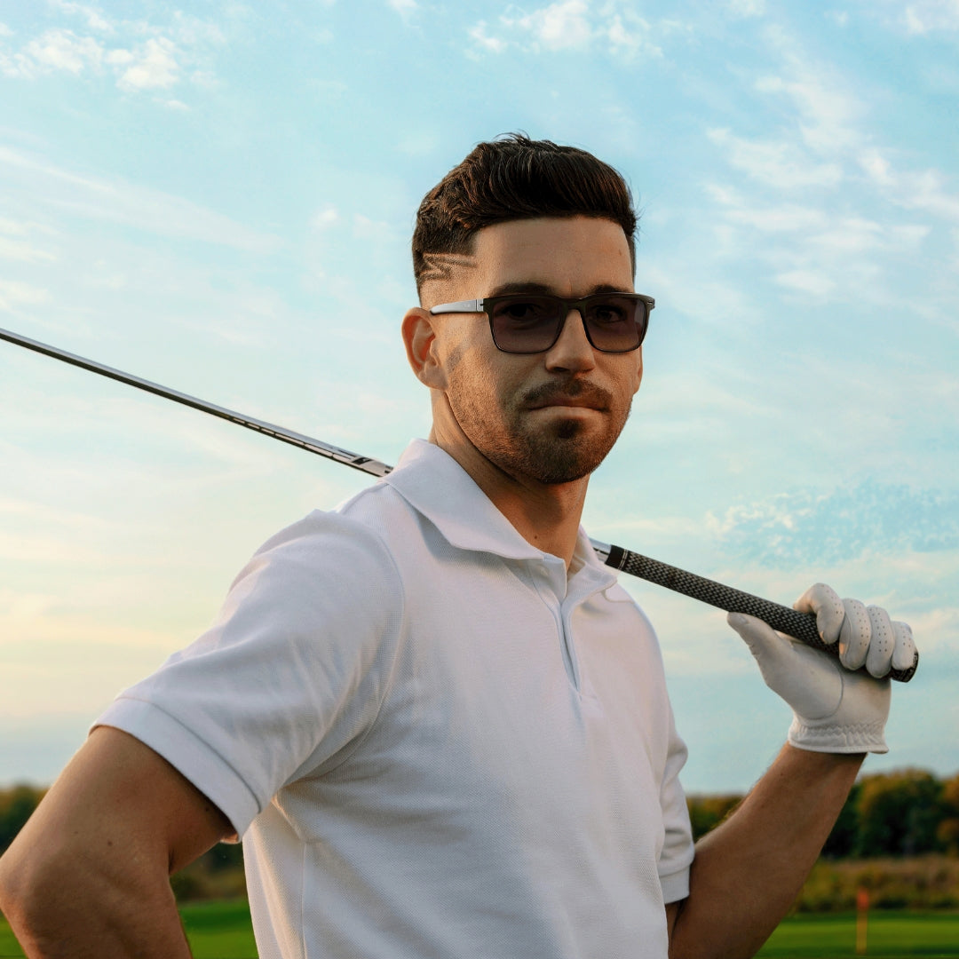 Man wearing golf sunglasses holding a golf club on a golf course with a clear sky