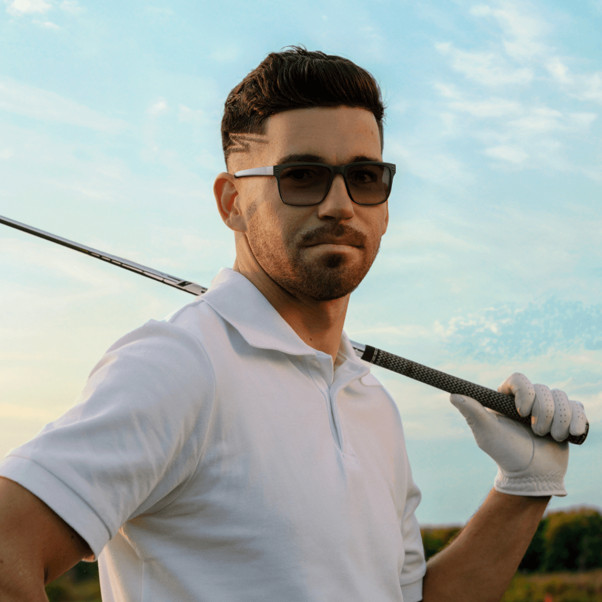 Black | Man wearing golf sunglasses holding a golf club on a golf course with a clear sky