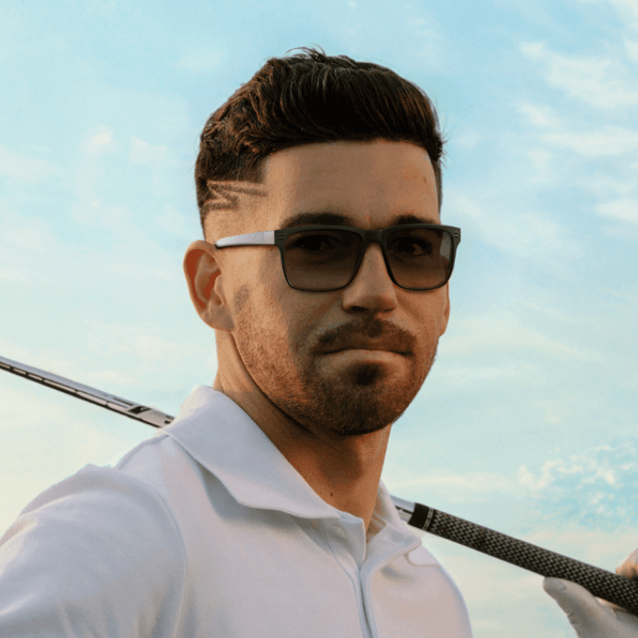 Matte Carbon | Man wearing golf sunglasses holding a golf club on a golf course with a clear sky