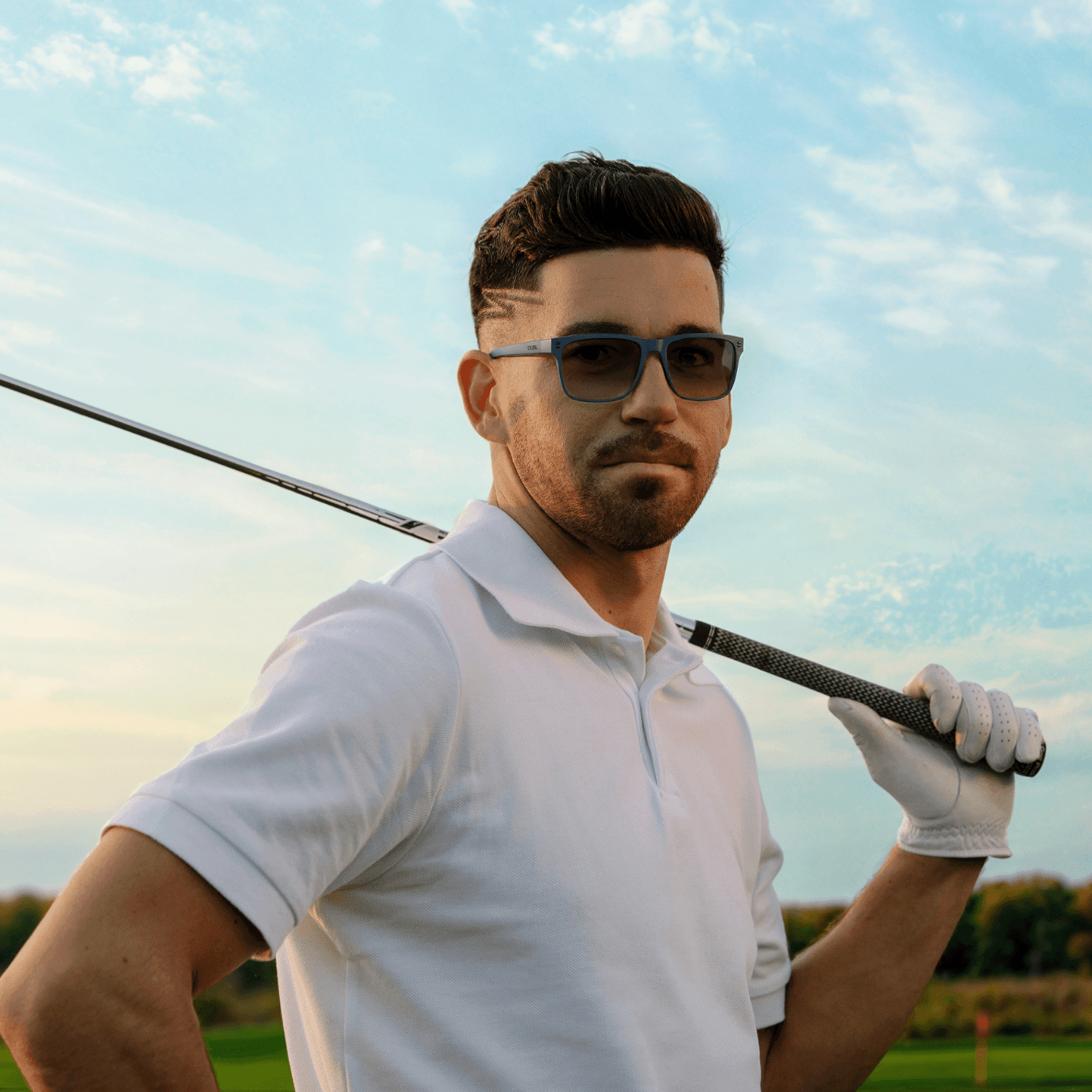 Navy | Man wearing golf sunglasses holding a golf club on a golf course with a clear sky